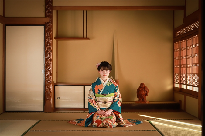 梅座敷で正座する青い振袖の女性