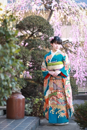 梅座敷の庭先に咲く枝垂れ梅のそばに佇む振袖姿の女性