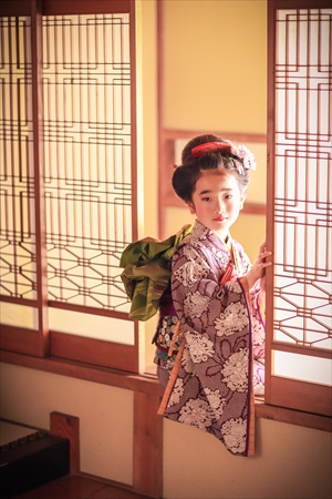 ガラス障子に腰かけてこちらを見る着物の女の子